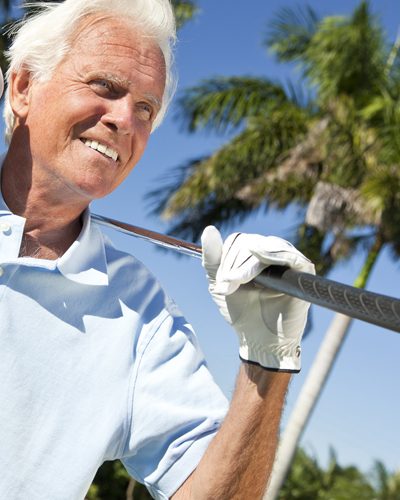 Man holding golf club with palm tree in background